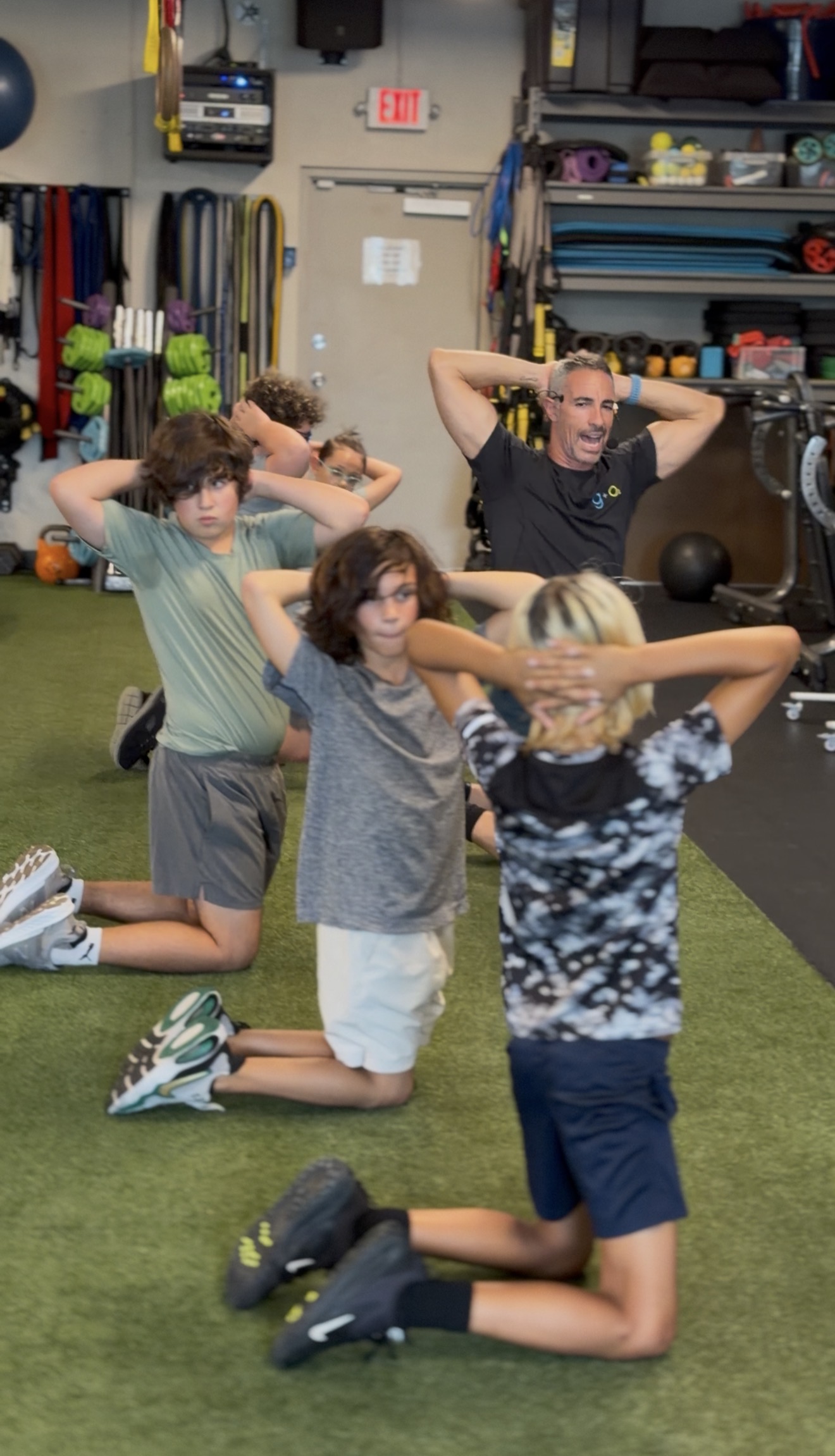 Coach and kids kneeling on the turf inside Gravity and Oxygen during Boca Youth Fit